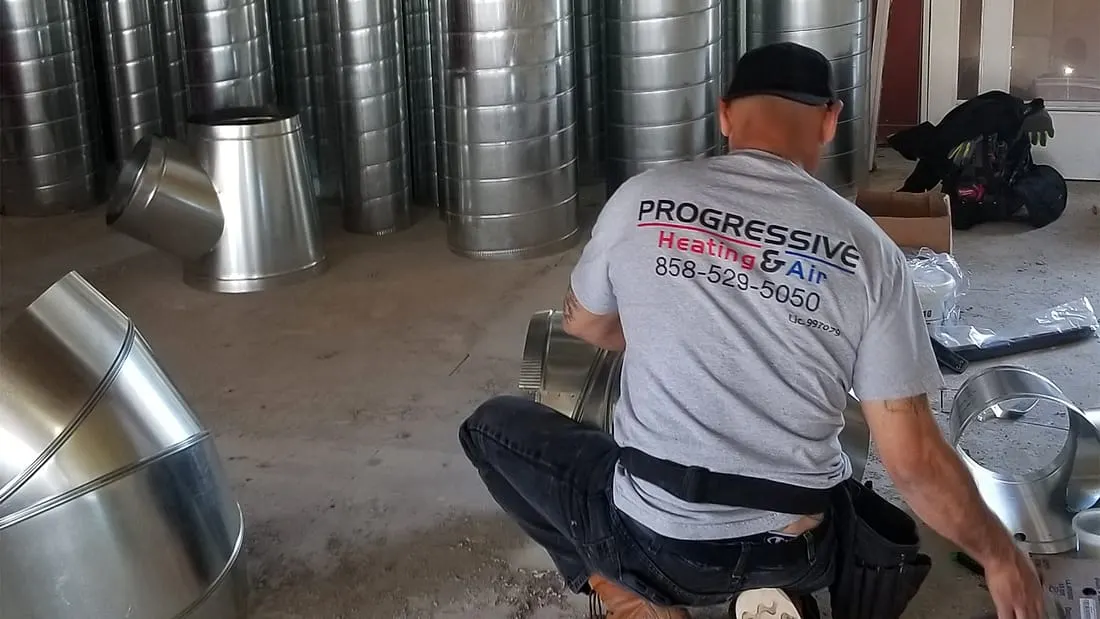 Progressive Heating & Air technician assembling ductwork on a San Diego job
